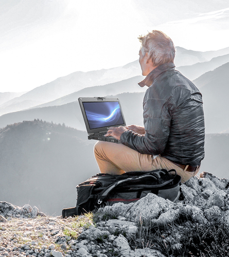 Man using a laptop against the backdrop of mountain peaks