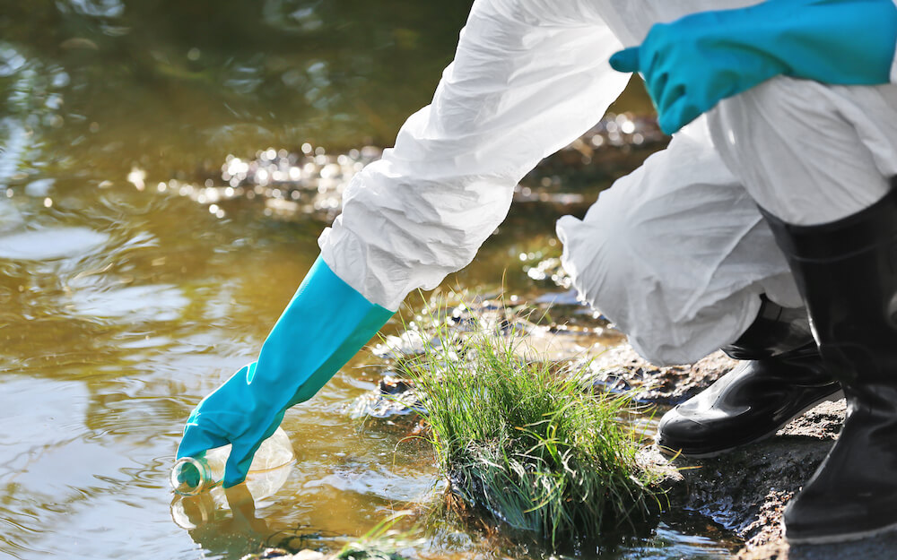 A person wearing protective clothing takes a water sample into a bottle